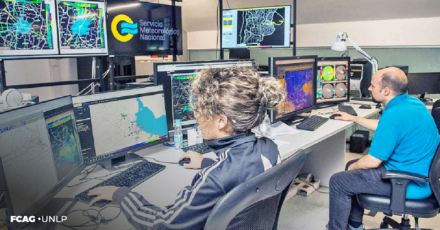 La imagen corresponde a una  oficina del SMN donde una mujer y un hombre están sentados frente a sus respectivas PC. Observan diferentes gráficos e imágenes vinculadas con la meteorología. 