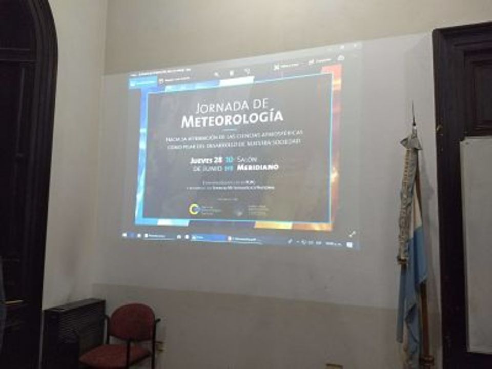 La imagen corresponde a una diapositiva proyectada en la pared del Salón de Actos, que lleva el título de la Jornada. Al costado se observa la bandera argentina que siempre está en el Salón Meridiano de nuestra Facultad.