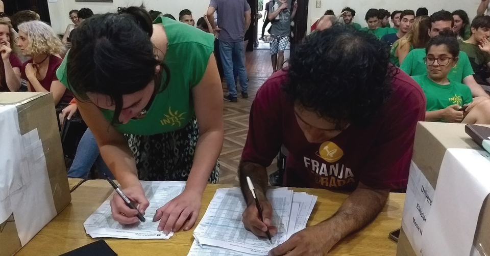 La imagen corresponde a dos estudiantes, uno por cada lista electoral, que revisan los padrones y  el número de votantes, antes de iniciar la apertura de urnas.