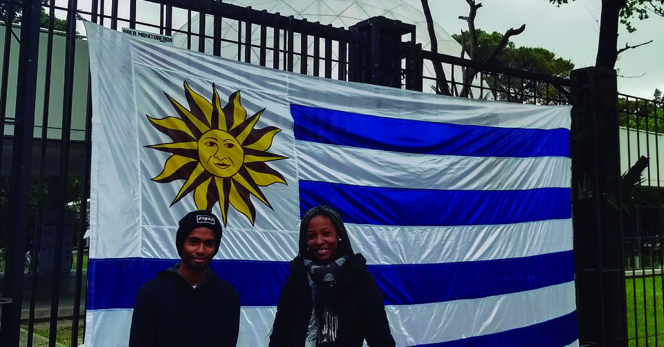 La imagen corresponde a dos estudiantes uruguayos que están delante de la bandera de su país, enganchada en las rejas de entrada al Planetario UNLP: Justo antes de iniciar el Congreso CONECTAR.