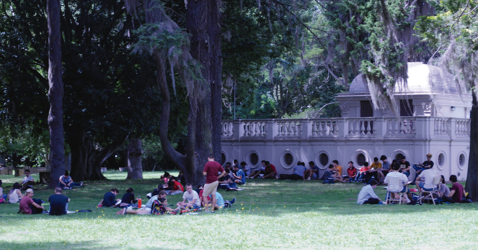 La imagen corresponde a estudiantes en el parque de la FCAG, sentados  en grupos. De fondo, se observa el  Pabellón Geofísico.  