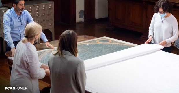 En la imagen se observa a un grupo de profesionales comenzando a desplegar el mapa del cielo sobre la mesa de la biblioteca FCAG.